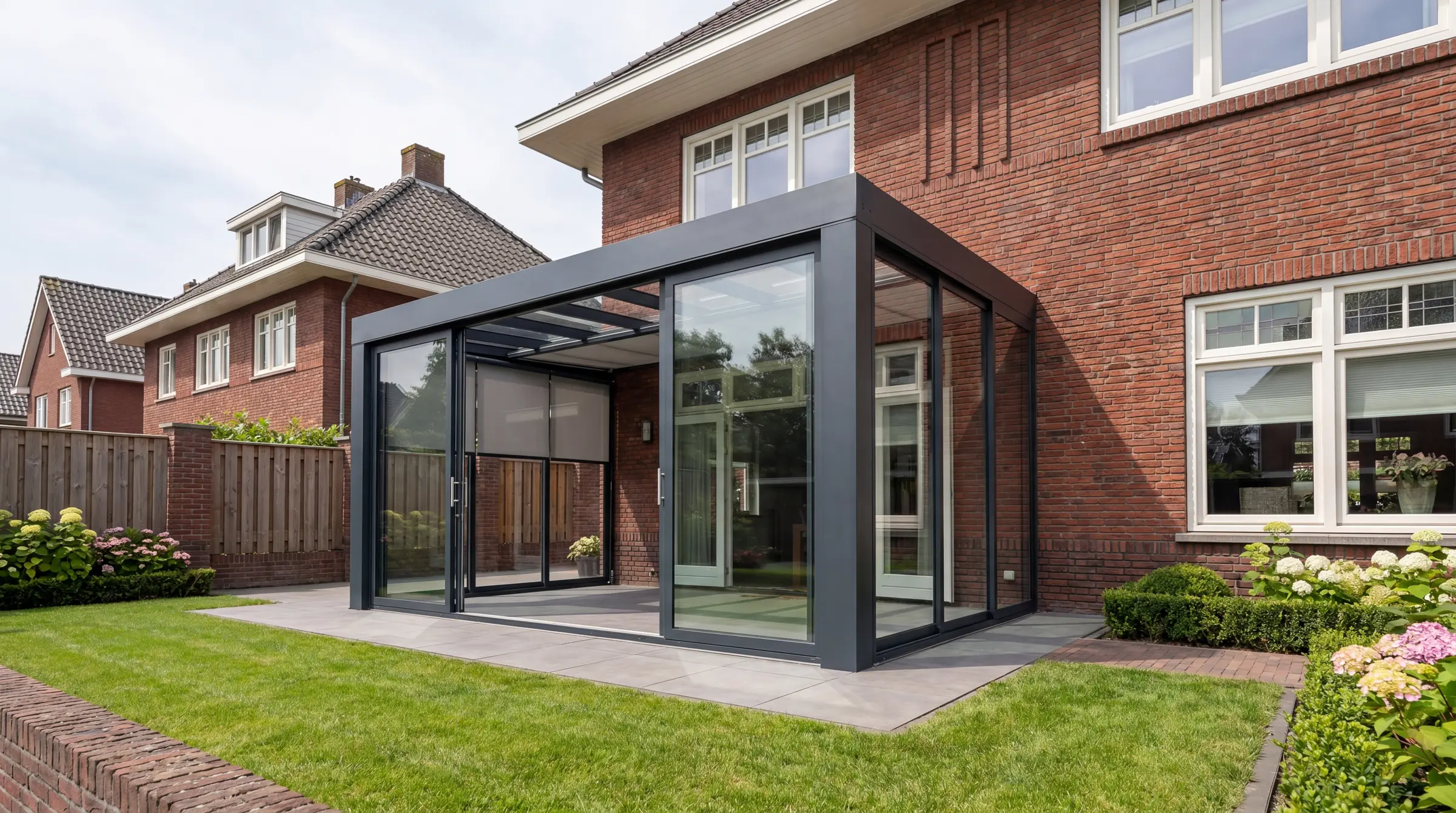 Verandera onderdakzonwering in antraciet veranda bij klassieke bakstenen woning — zonweringdoek onder het glazen dak voor beschutte plaatsing